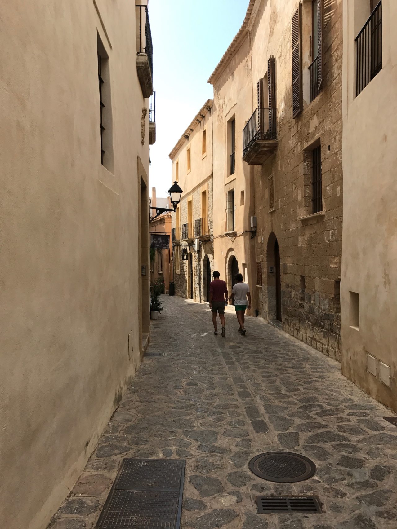 Narrow Street With Doors And Windows And People Walking On Cobblestone