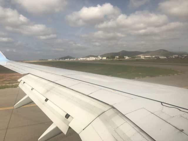 View Of Airplane Wing On Runway With Cloudy Sky