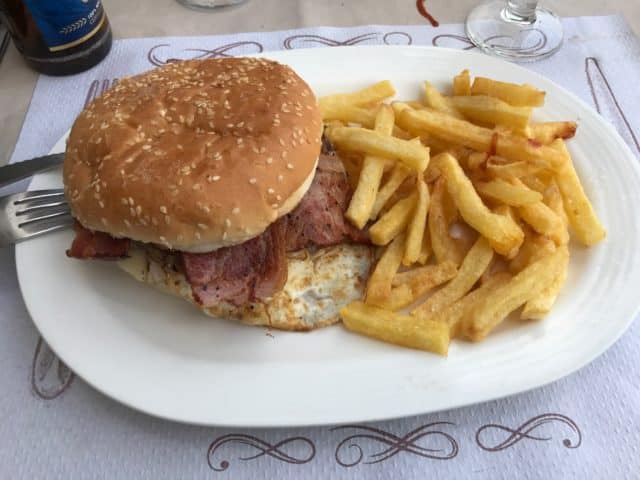 A Hamburger Of Beef With Bacon Slices And Fried Eggs And Salted French Fries On A White Plate