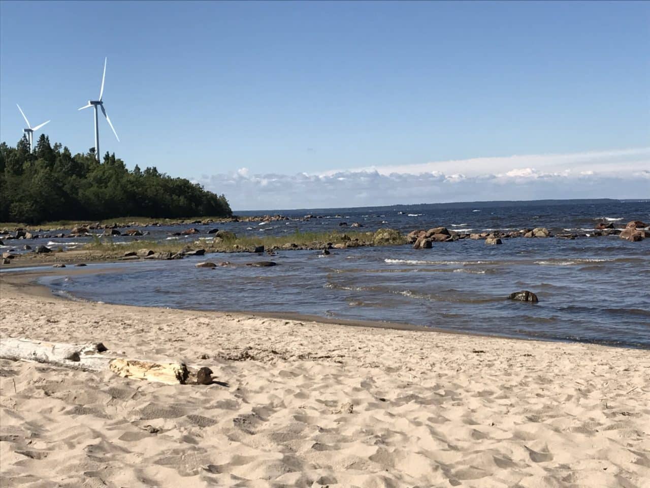Sand And Rocks On Beach With Two Windmills In The Background