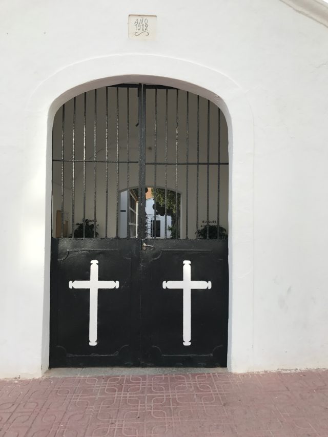 Black Steel Door With White Crosses And Grille At Cemetery With Red Stone Slabs On The Ground