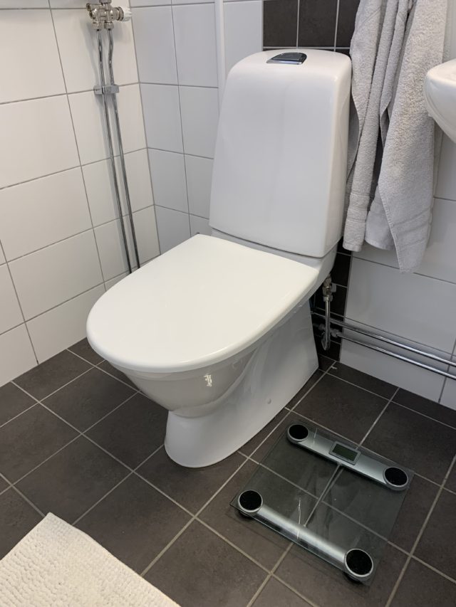 Clean Bathroom With A White Toilet And A Scale On The Floor