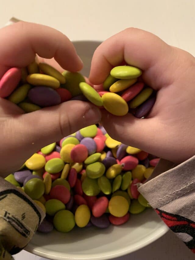 Child Holding Multi Color Candy Over Bowl
