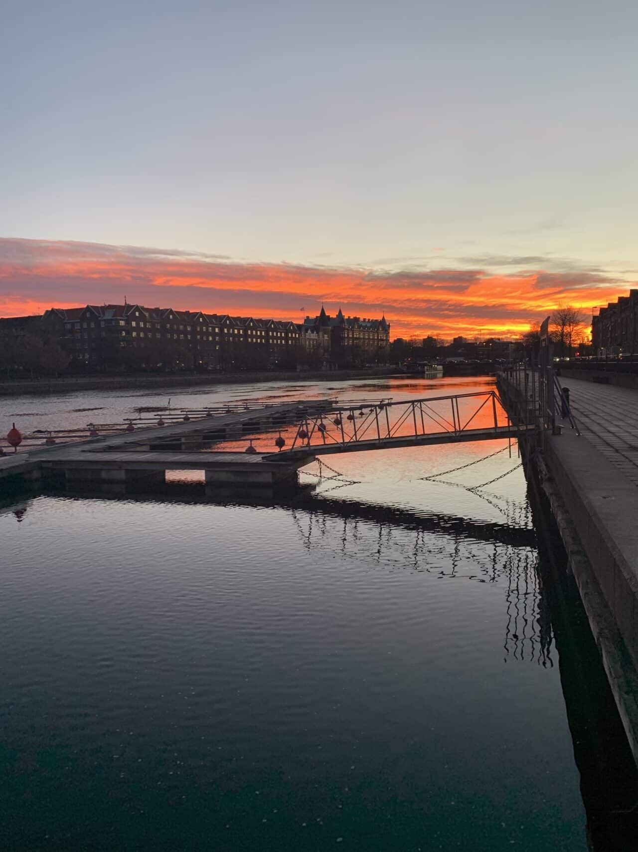 Dock Bridge In City River With Orange Sunset Sky