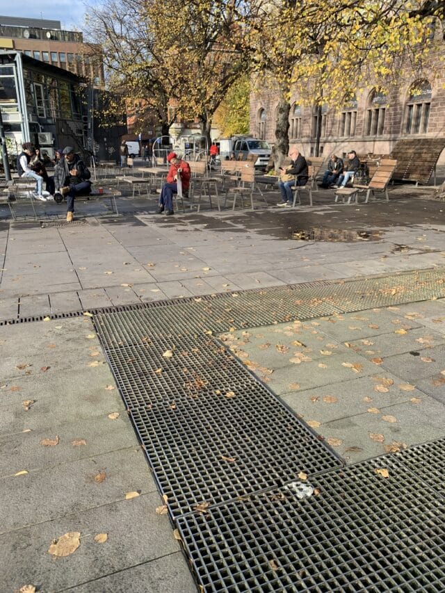 People Sitting On Park Benches On City Square